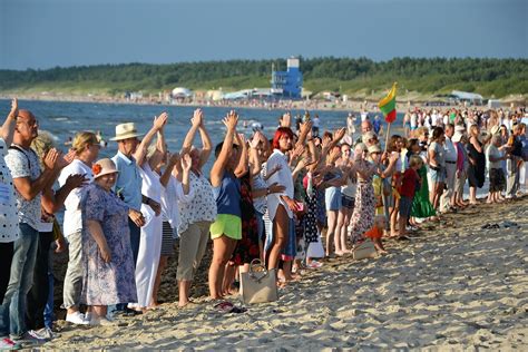 Simbolinis atvaizdas - du žmonės rankomis susikabine, žiūrintys į saulėlydį