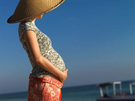 Nėščia moteris su skėčiu nuo saulės paplūdimyje