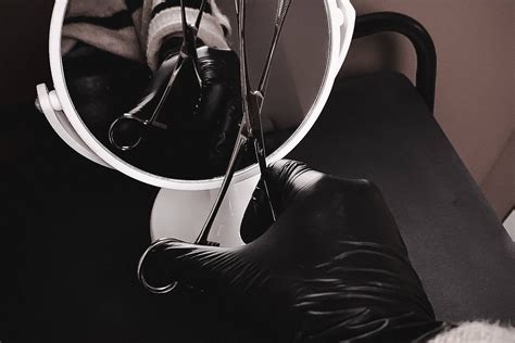 Nuotrauka, kurioje meistras, dėvintis pirštines ir kaukę, atlieka auskarų vėrimą