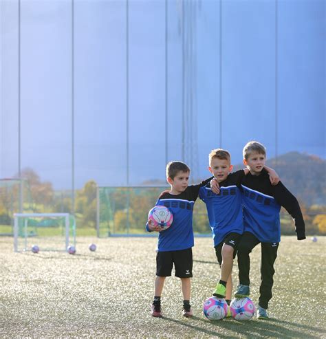 Vaiko rankos ir kojos dėvinčios sportinius šortus ir sportbačius, žaidžiančios futbolą lauke.