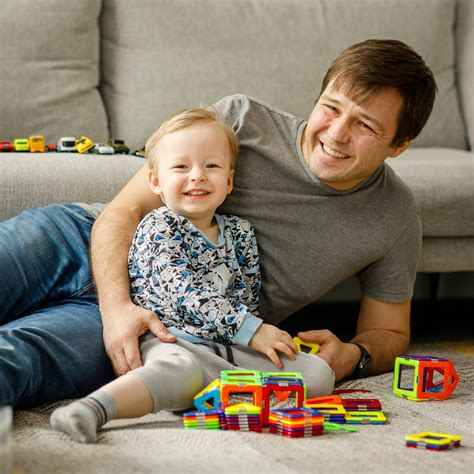 Mama glaudžia mažą vaiką, šalia žaidžia du vyresni